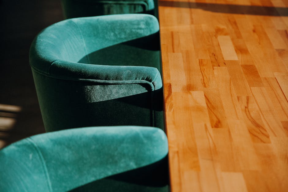 A long, bright blue, upholstered bench with a smooth, clean surface is positioned against a plain white wall in a well-lit room. The seating area features rectangular cushions with visible seams, and the upholstery material appears to be vinyl or faux leather, contributing to its shiny, maintained look. The floor beneath the bench is covered with large, light gray ceramic tiles, which are also clean and glossy. The room has a minimalist setup, emphasizing the cleanliness and tidy appearance consistent with professional surface cleaning and sanitisation services offered by Carpet Cleaners Edgware, specializing in domestic cleaning for homes on Burnt Oak Broadway, EDGWARE.